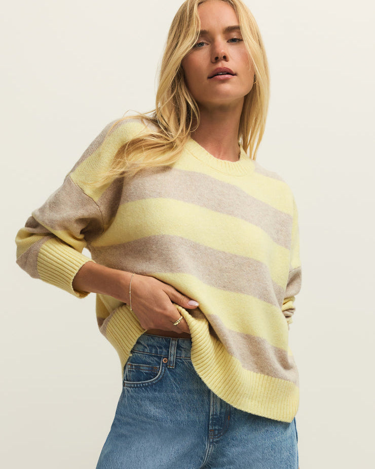 Woman wearing a yellow and brown striped sweater with blue jeans on a plain background