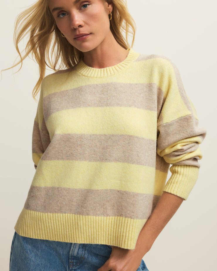 Woman wearing a yellow and gray striped sweater with blue jeans on a plain background