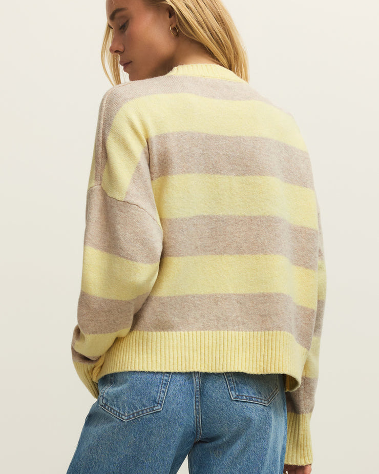 Woman wearing a yellow and gray striped sweater with blue jeans on a plain background