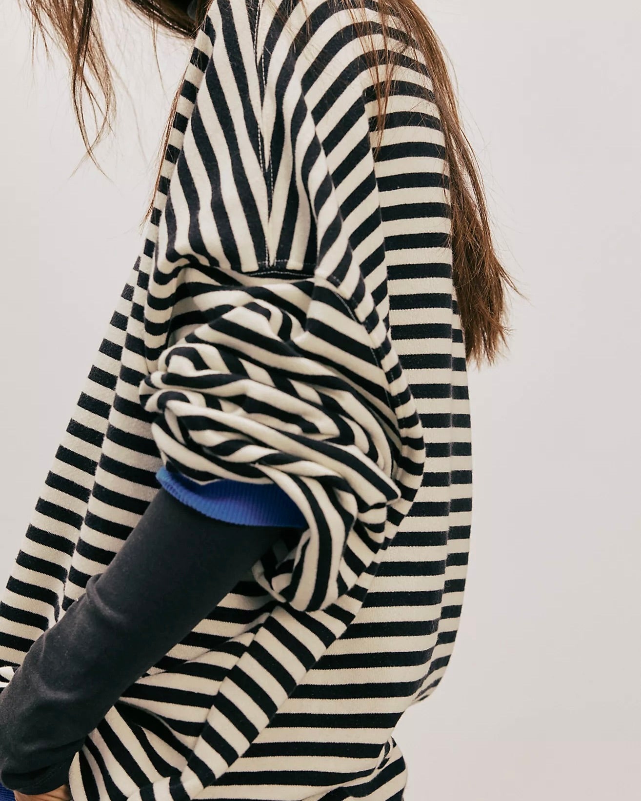 Side view of model standing wearing the Free People Classic Striped Oversized Crewneck in front of a white wall.