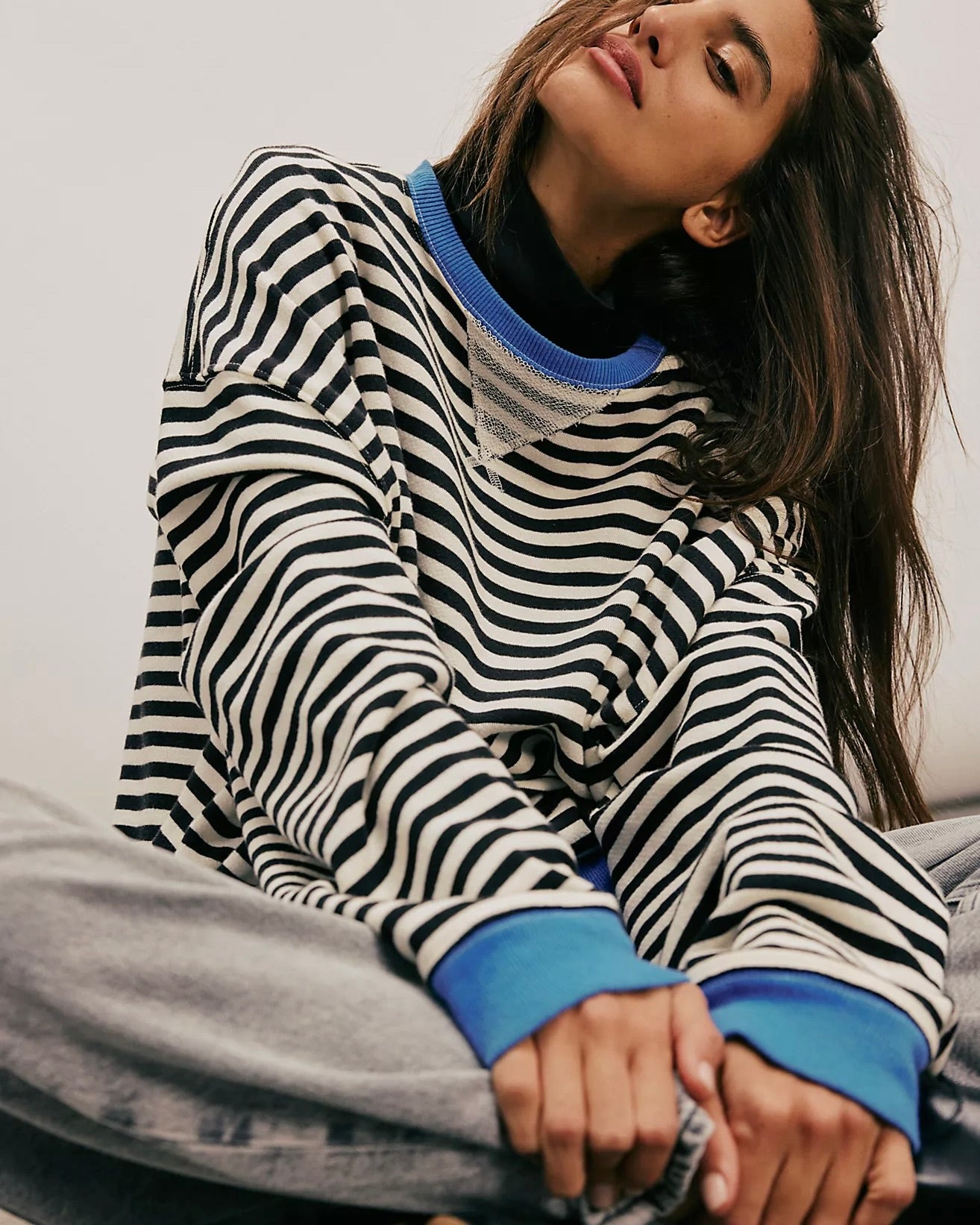 Front view of model sitting wearing the Free People Classic Striped Oversized Crewneck in front of a white wall. 