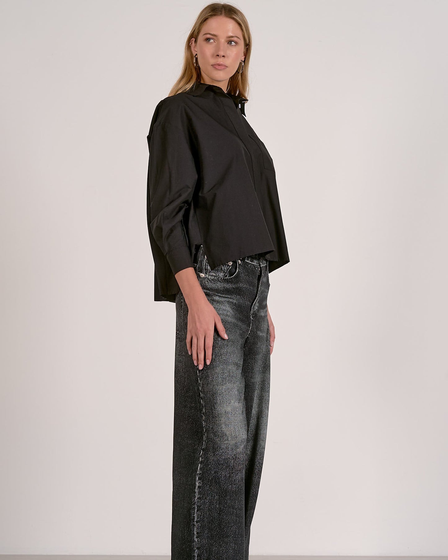 Woman wearing a black blouse and gray jeans against a white background