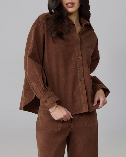 A woman wearing a matching brown corduroy button-up shirt and pants set, photographed against a plain light gray studio background.