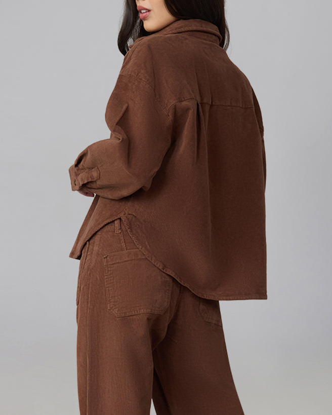 A model shown from the back wearing a brown corduroy button-up shirt and matching brown corduroy trousers against a solid gray studio background.