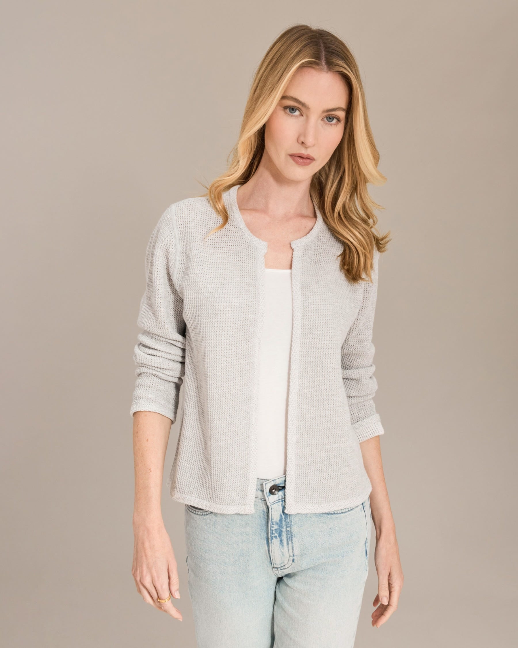 Woman wearing a light gray cardigan over a white shirt with light blue jeans on a beige background