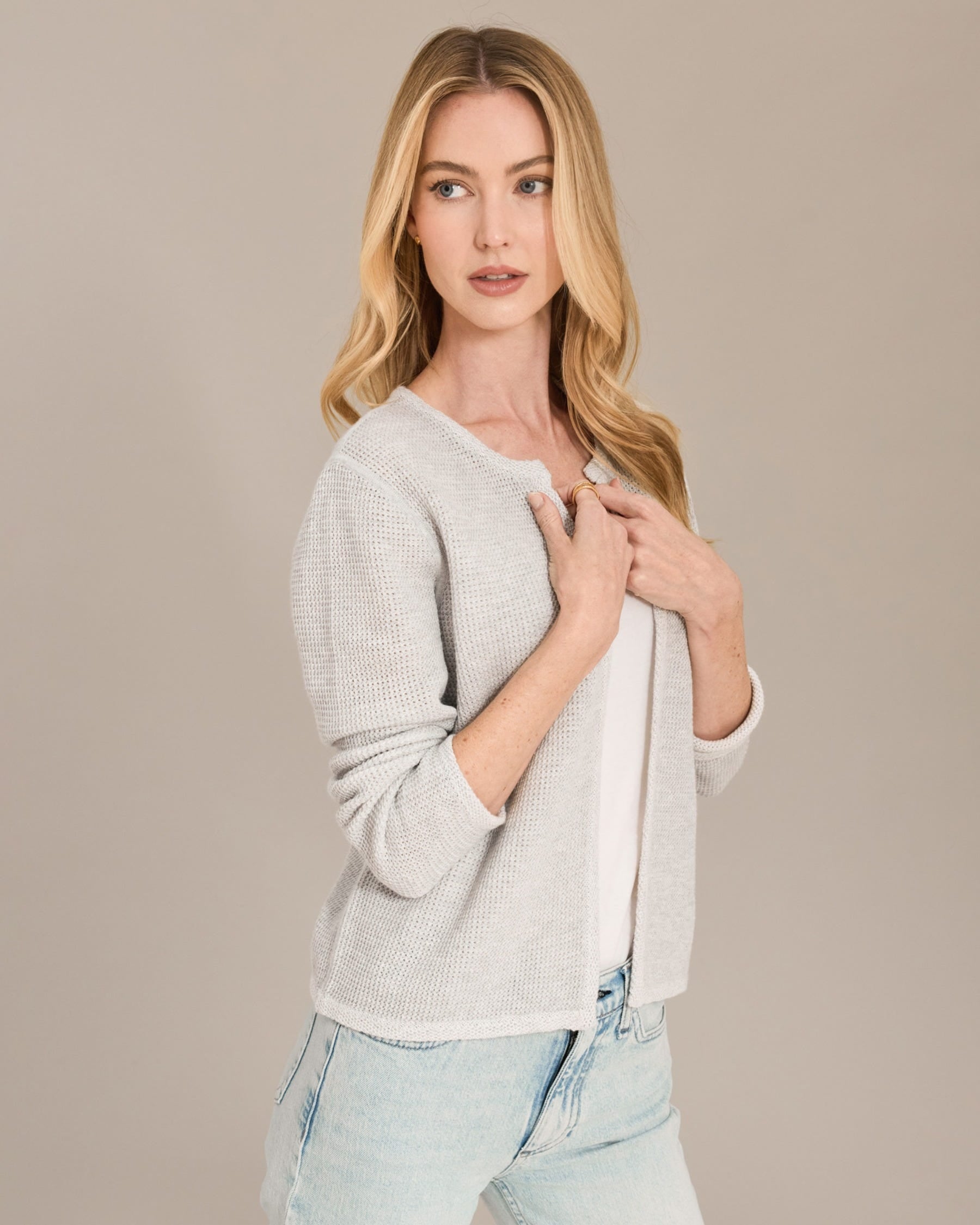 Woman wearing a light gray sweater and jeans against a beige background
