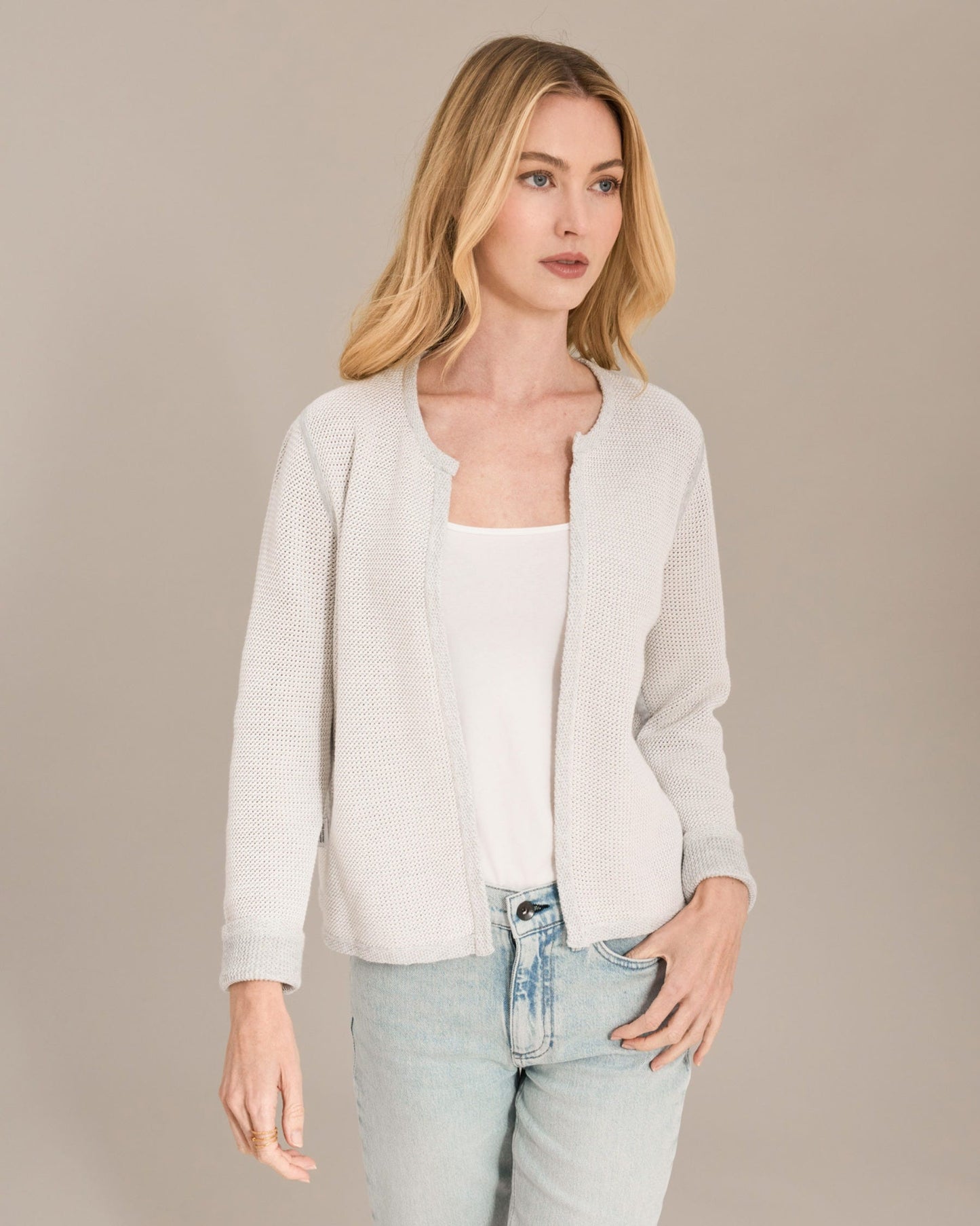 Woman wearing a light gray cardigan over a white top and light blue jeans on a beige background