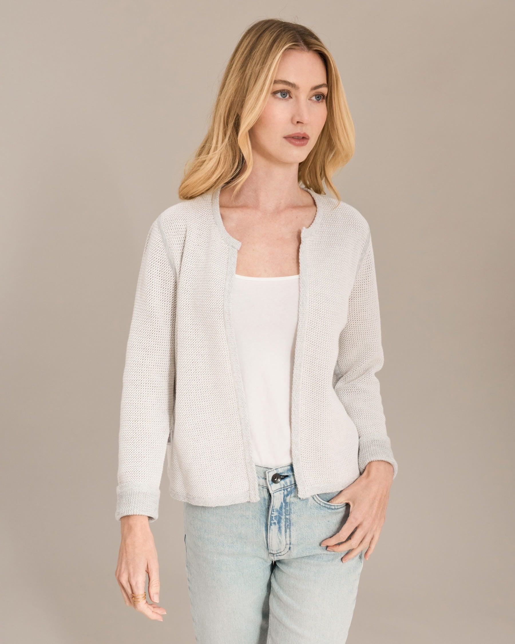 Woman wearing a light gray cardigan over a white top and light blue jeans on a beige background