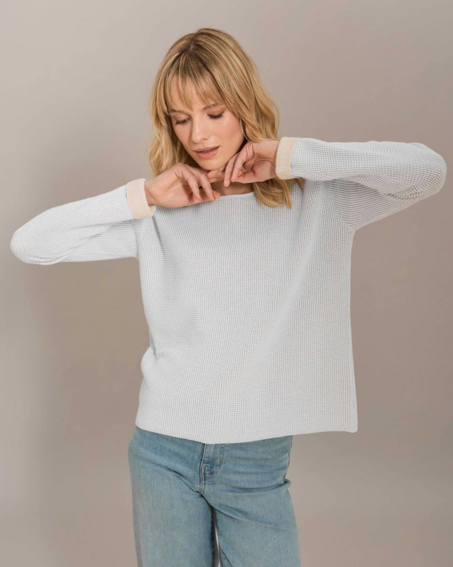 Woman wearing a light gray sweater and blue jeans against a plain background