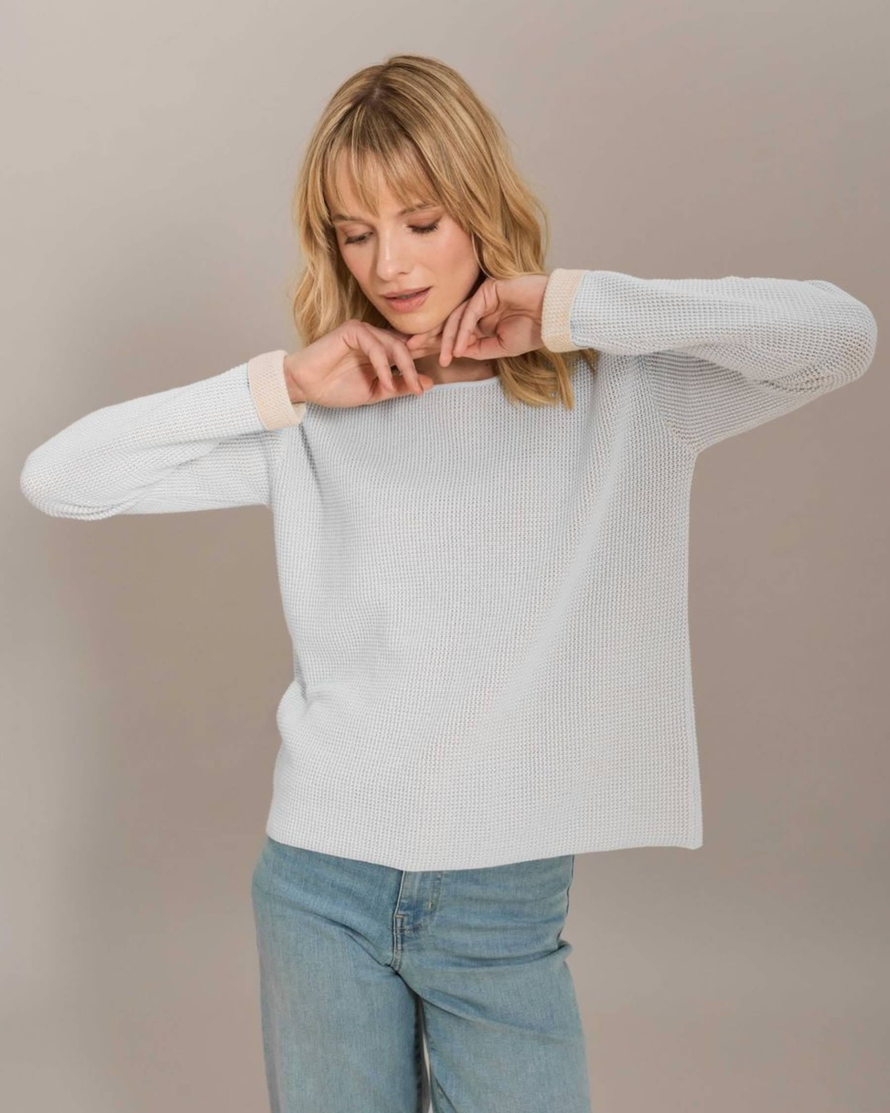 Woman wearing a light gray sweater and blue jeans against a plain background