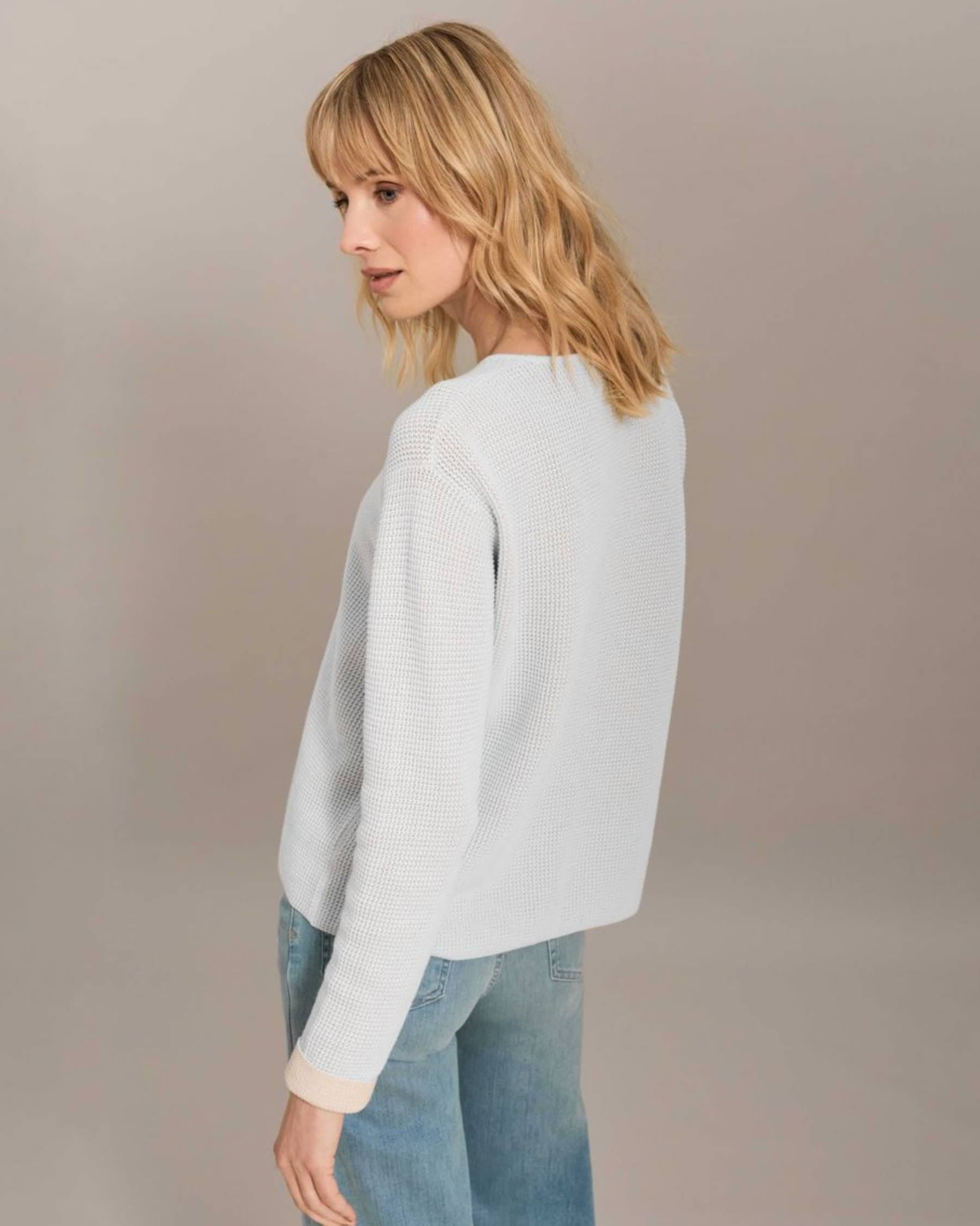 Woman wearing a light gray sweater and blue jeans against a plain background