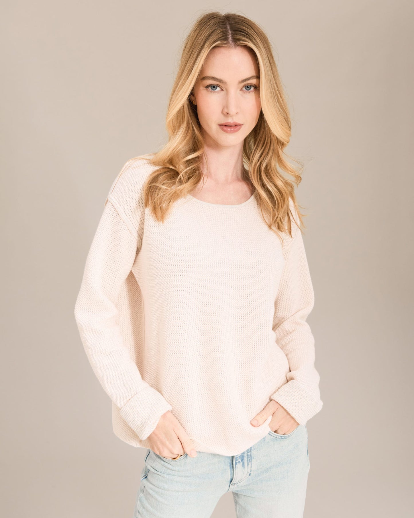Woman wearing a light pink sweater and light blue jeans against a beige background