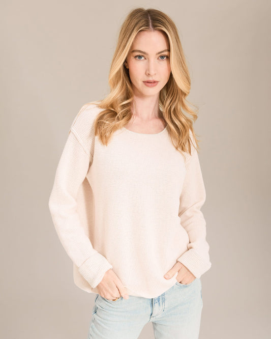Woman wearing a light pink sweater and light blue jeans against a beige background