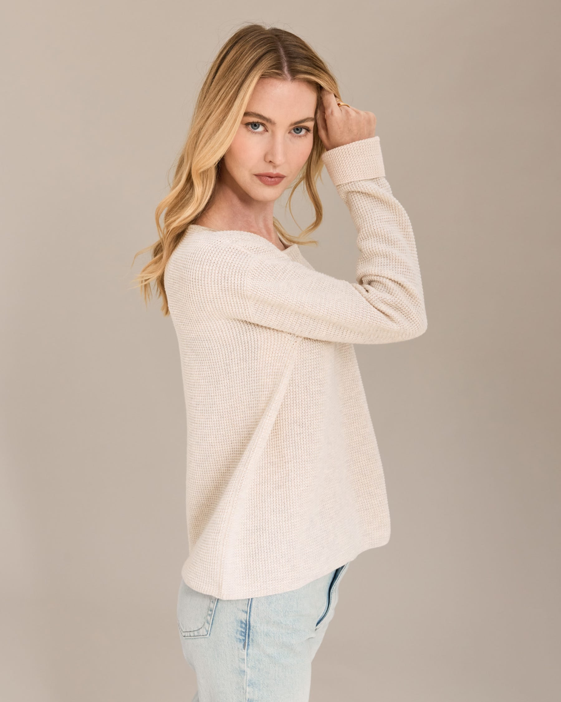 Woman wearing a beige sweater and light blue jeans against a beige background