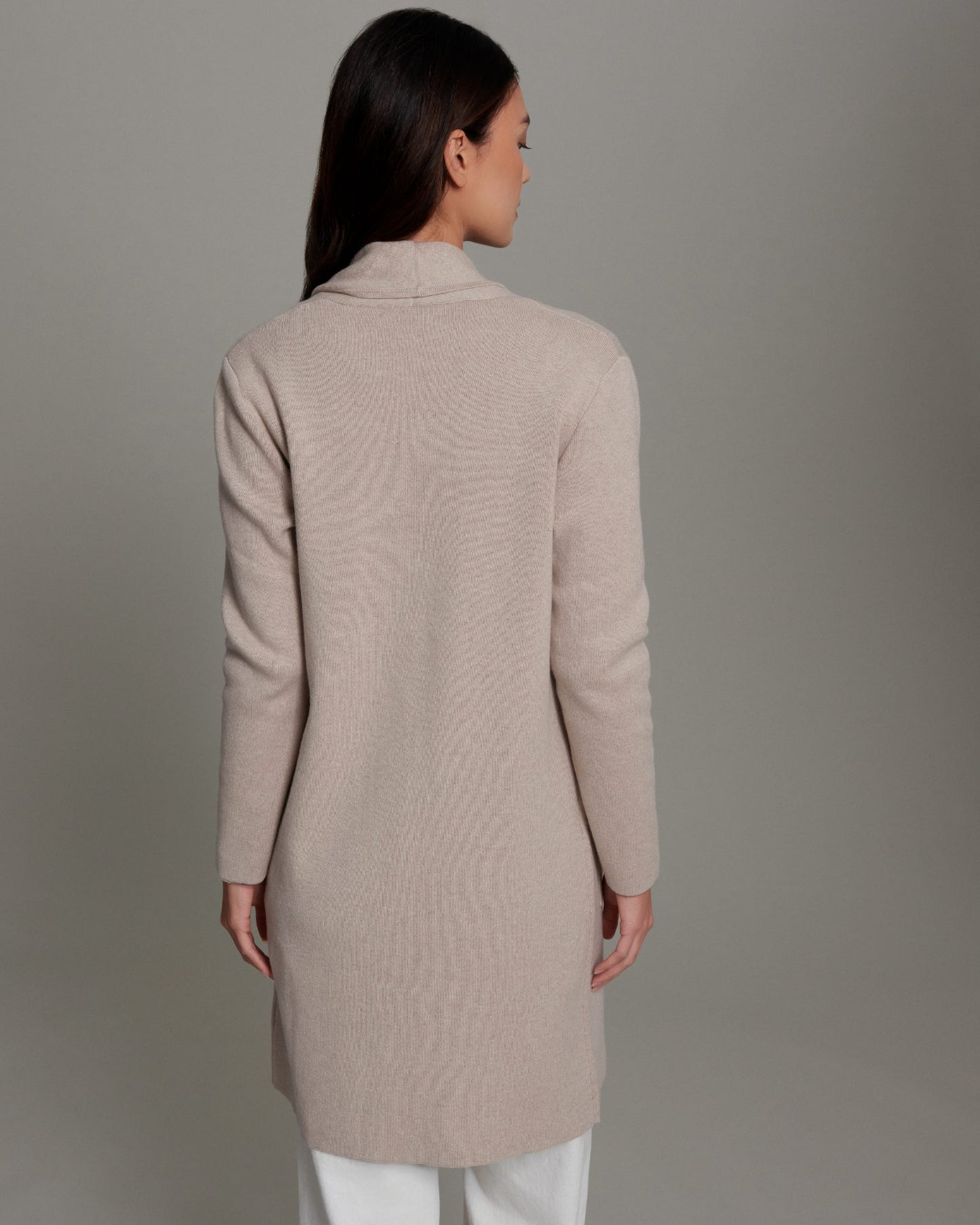 Woman wearing a beige long coat against a gray background