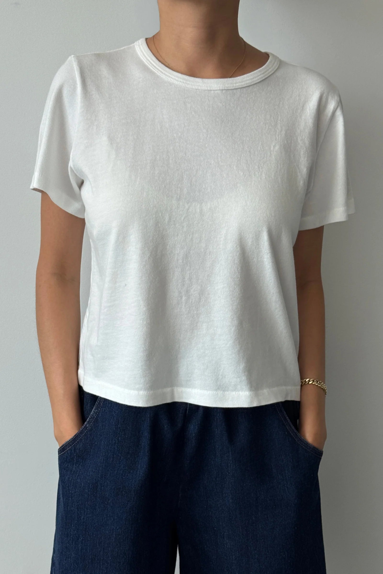 Person wearing a plain white t-shirt and dark pants against a neutral background