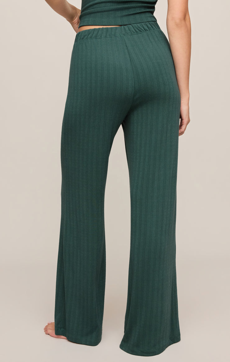 A person wearing dark green wide-leg pants with a subtle vertical textured stripe pattern, shown from the back against a plain beige studio background.