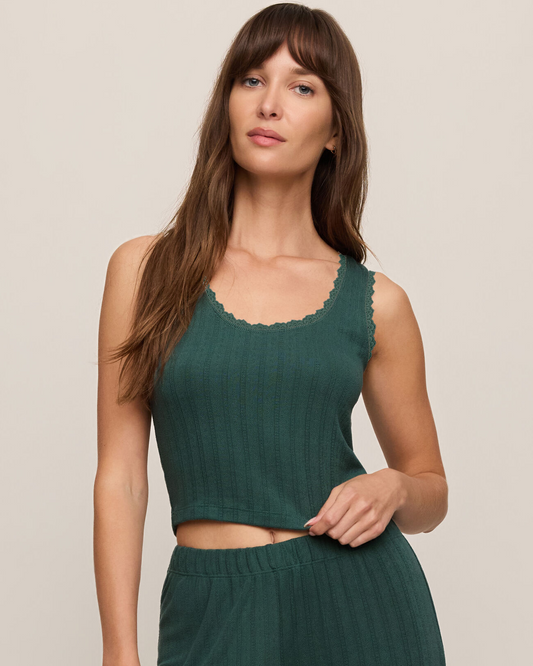 A woman modeling a matching two-piece ribbed lounge set in a deep teal green color, featuring a sleeveless scoop-neck crop top with scalloped trim and high-waisted pants, against a solid light beige background.