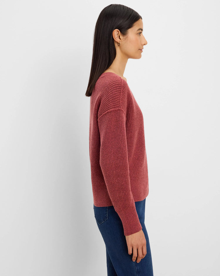 A woman shown in side profile wearing a ribbed knit long-sleeve sweater in a dusty rose color, paired with dark blue jeans, against a plain light gray background.