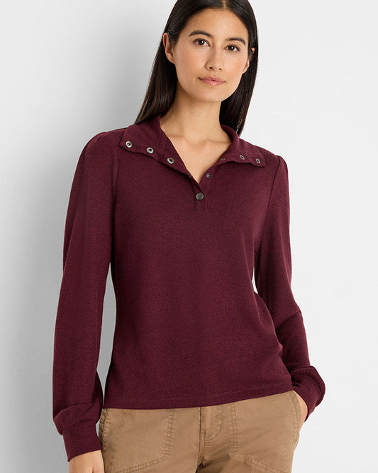 A woman modeling a long-sleeve knit polo-style top in deep burgundy with a buttoned collar and tan pants, photographed against a light gray studio background.
