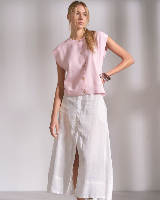 Woman wearing a pink top and white pants on a plain background