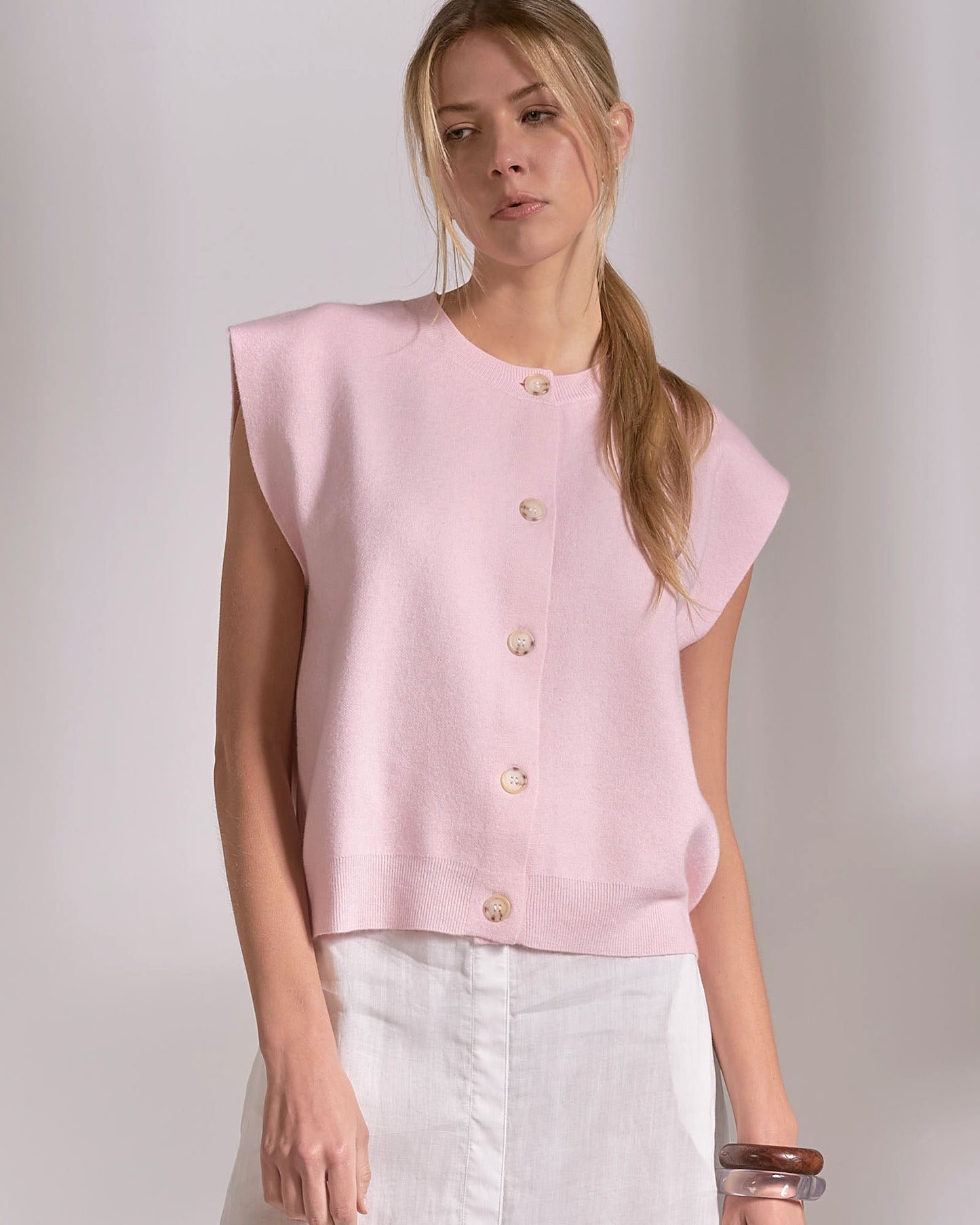 Woman wearing a light pink sleeveless blouse with buttons on a plain background