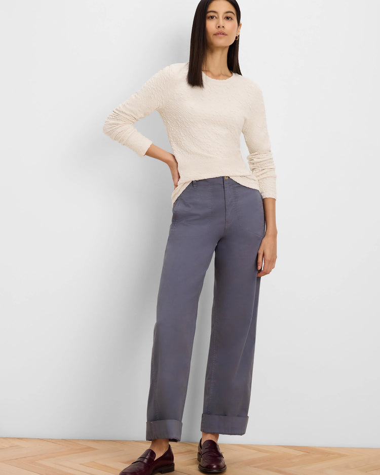 A woman modeling a cream ribbed long-sleeve top and slate blue wide-leg trousers with dark brown leather loafers, standing against a light gray wall on a light wood floor.