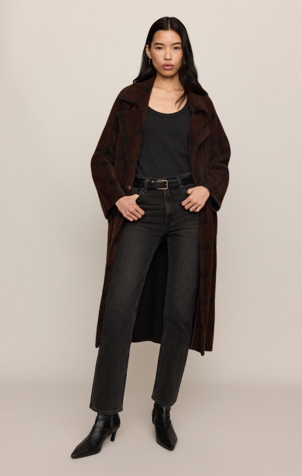 Woman wearing a brown coat, black top, and jeans on a beige background