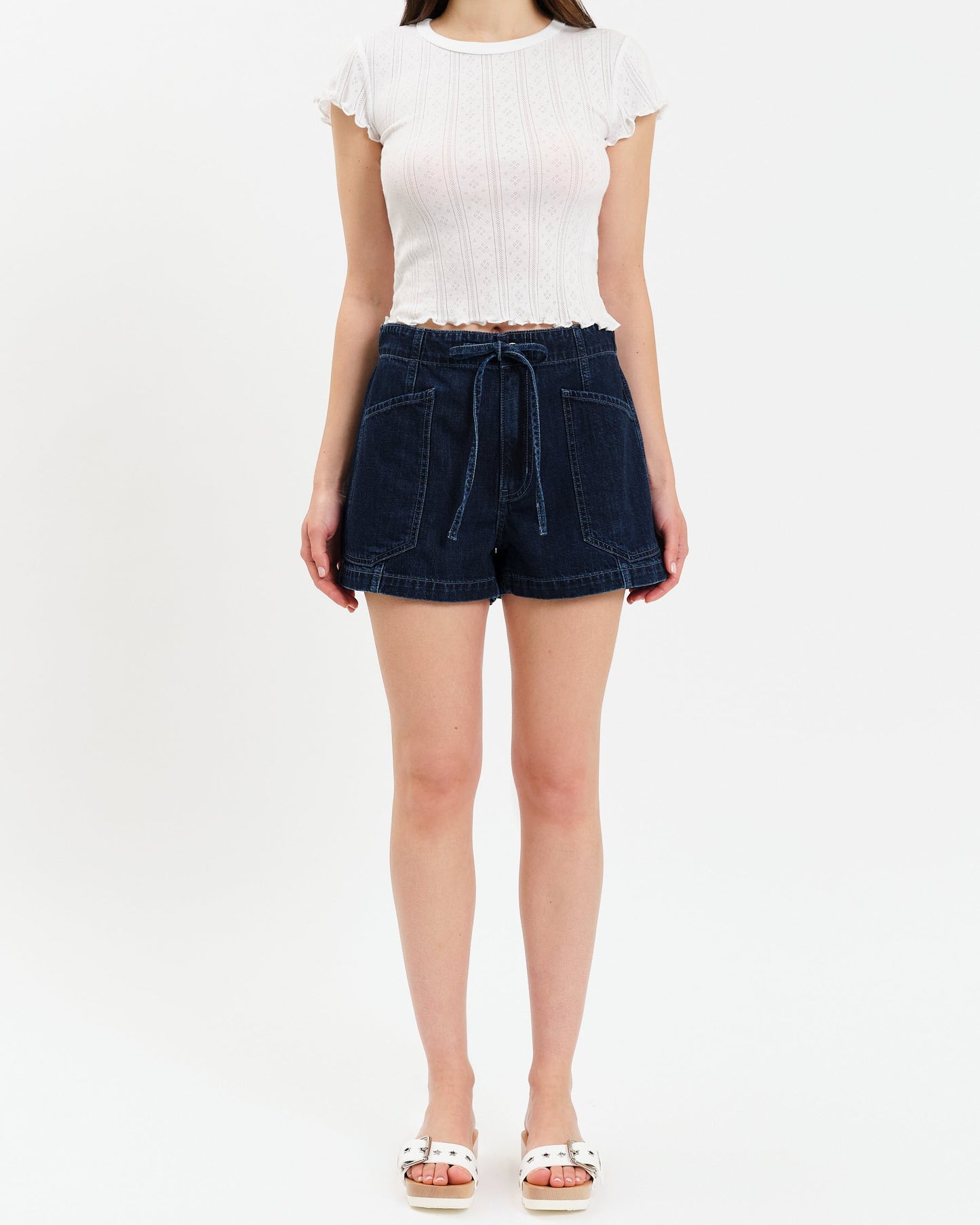 Person wearing a white top and dark denim shorts on a white background
