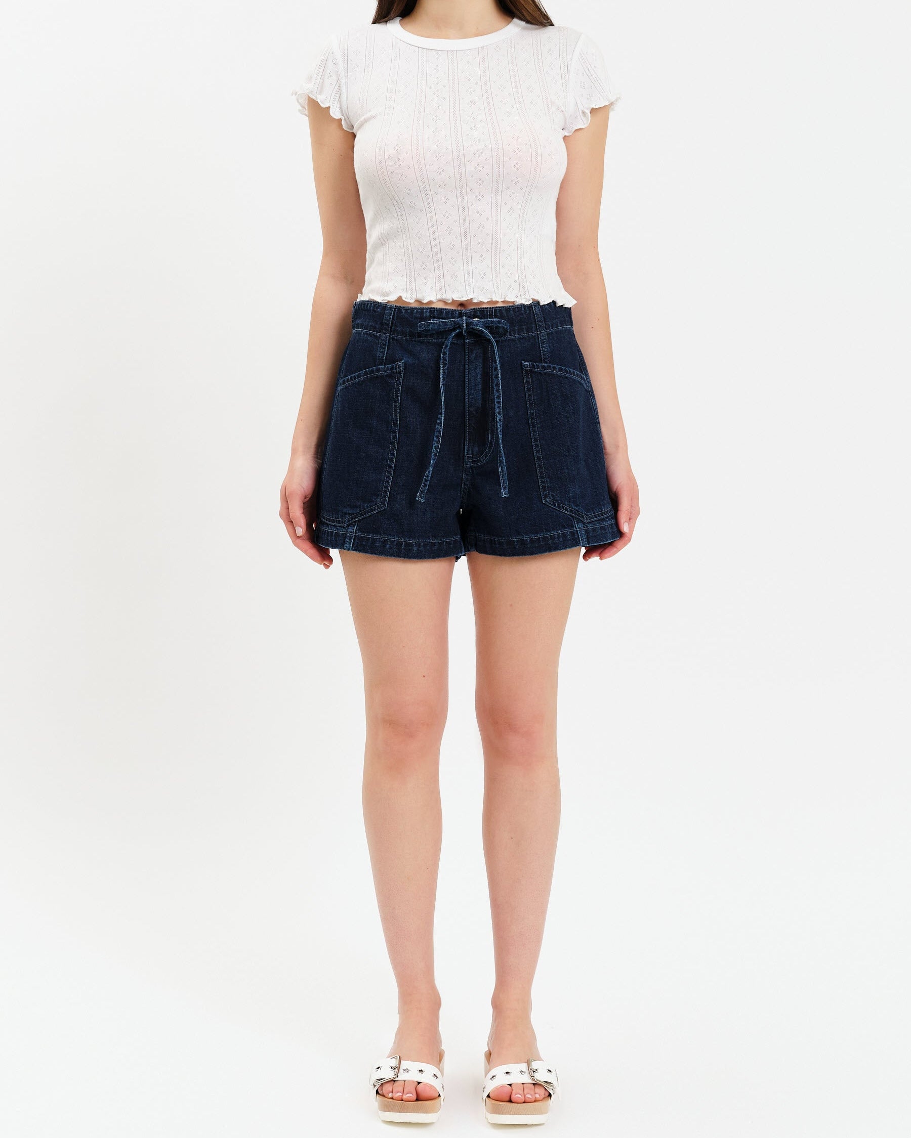 Person wearing a white top and dark denim shorts on a white background