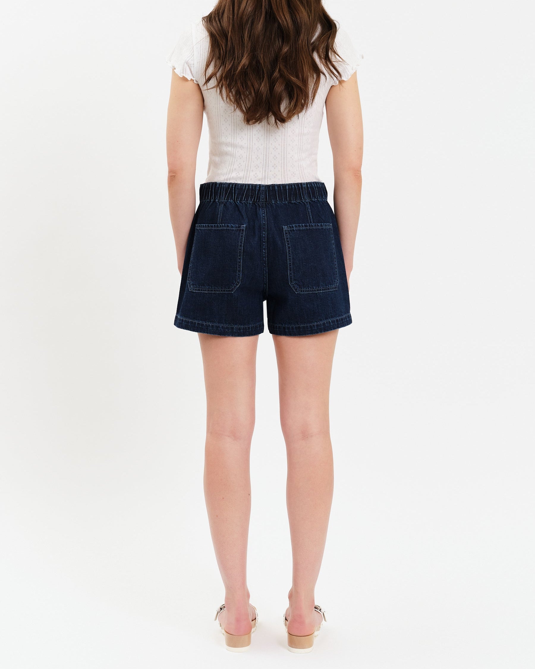 Person wearing a white top and dark denim shorts on a white background