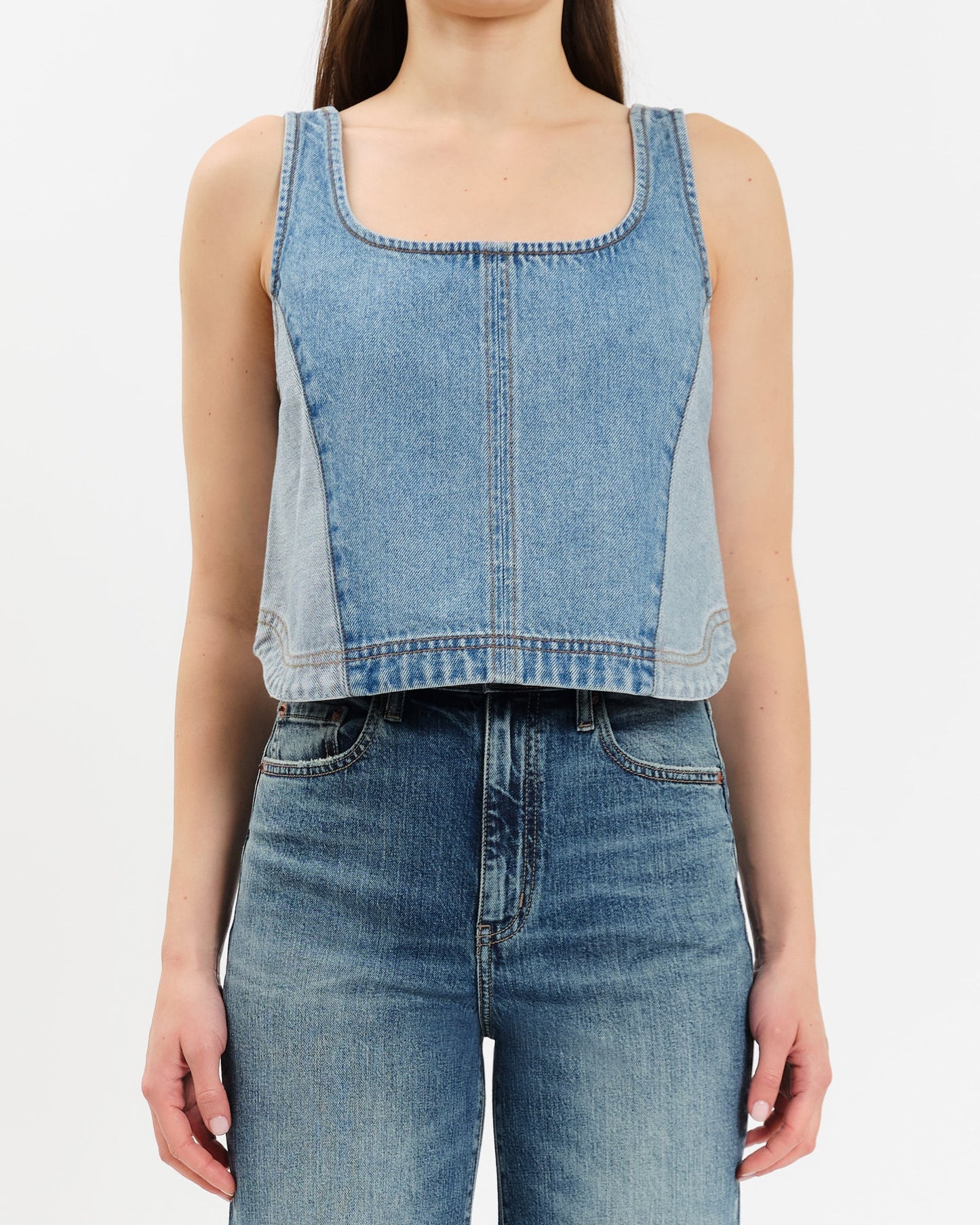 Person wearing a denim sleeveless top and high-waisted jeans on a white background