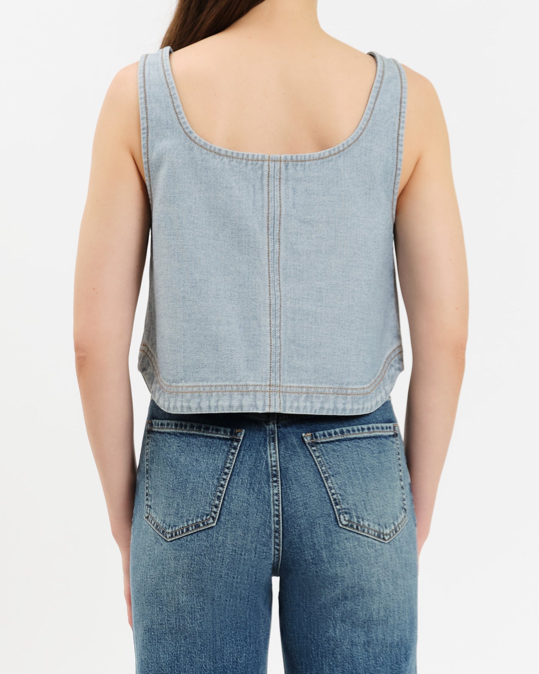 Person wearing a light blue denim tank top and jeans on a white background
