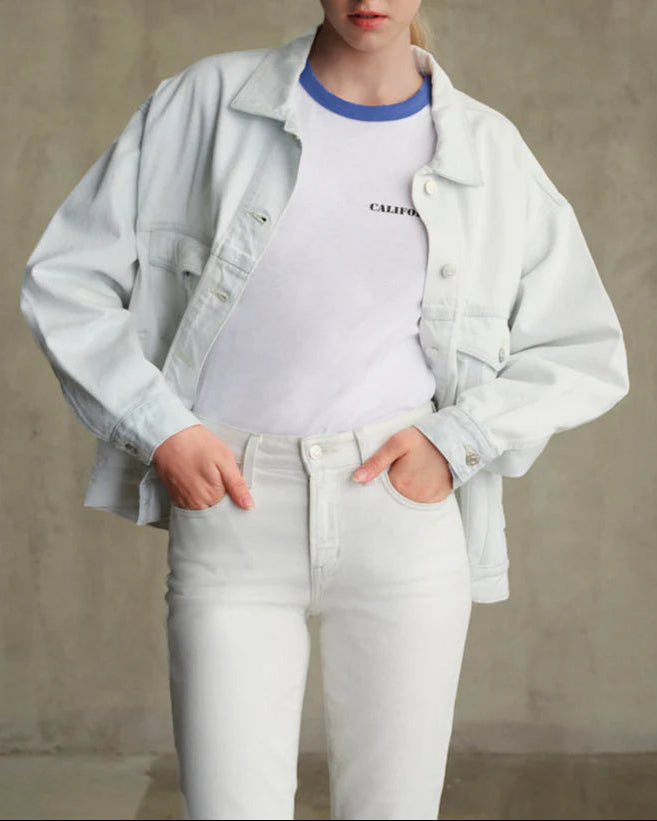 Person wearing a light gray jacket over a white shirt, paired with white pants against a neutral background.