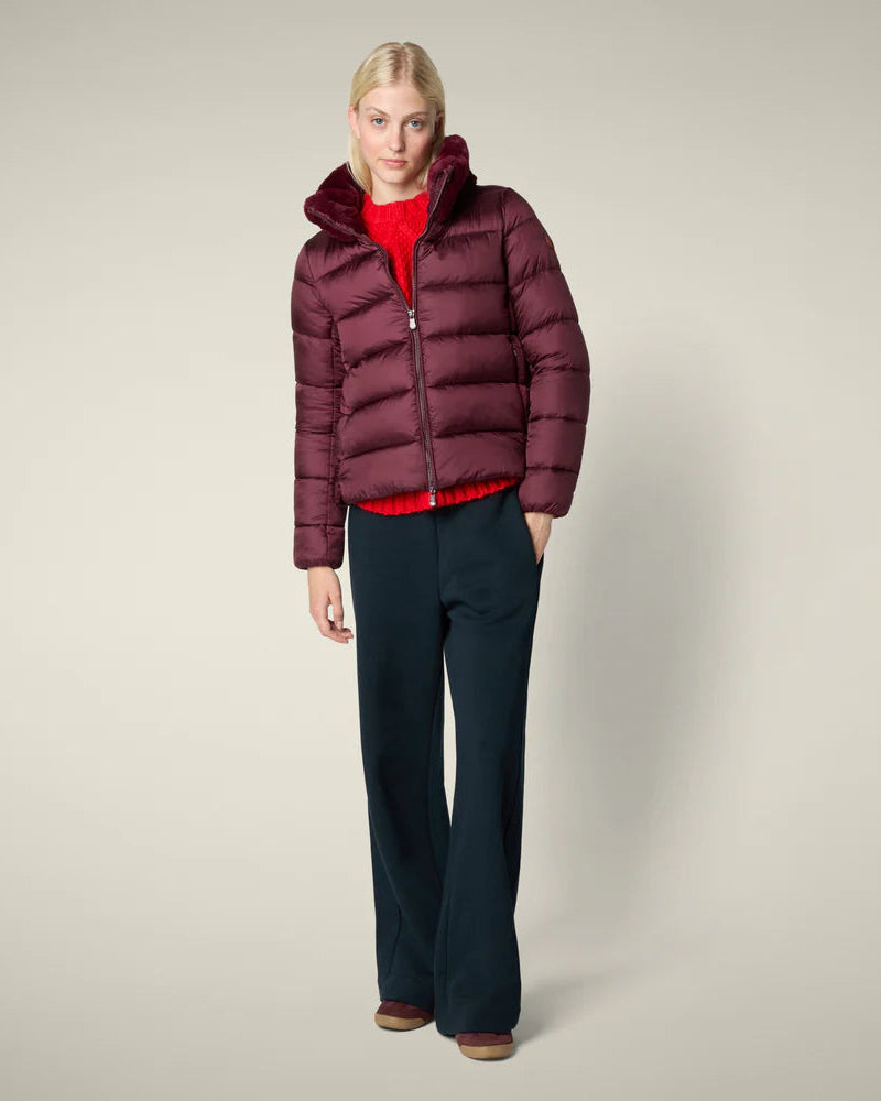 Woman wearing a burgundy puffer jacket on a beige background
