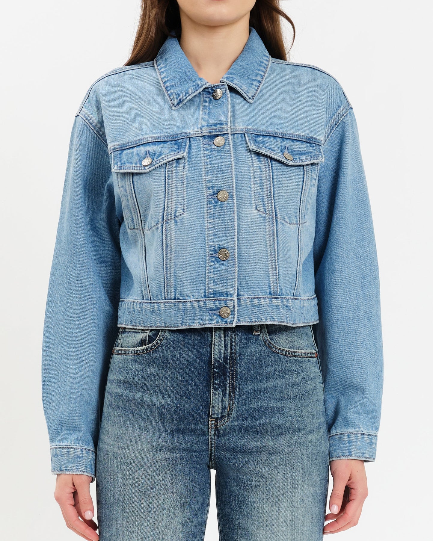 Person wearing a light blue denim jacket and jeans on a white background