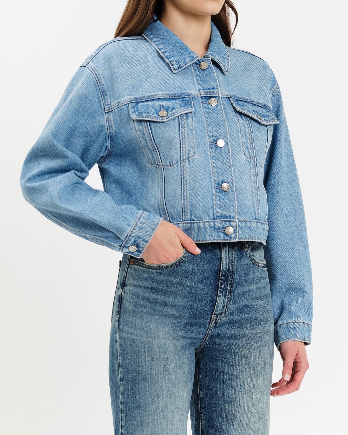 Person wearing a light blue denim jacket and jeans on a white background