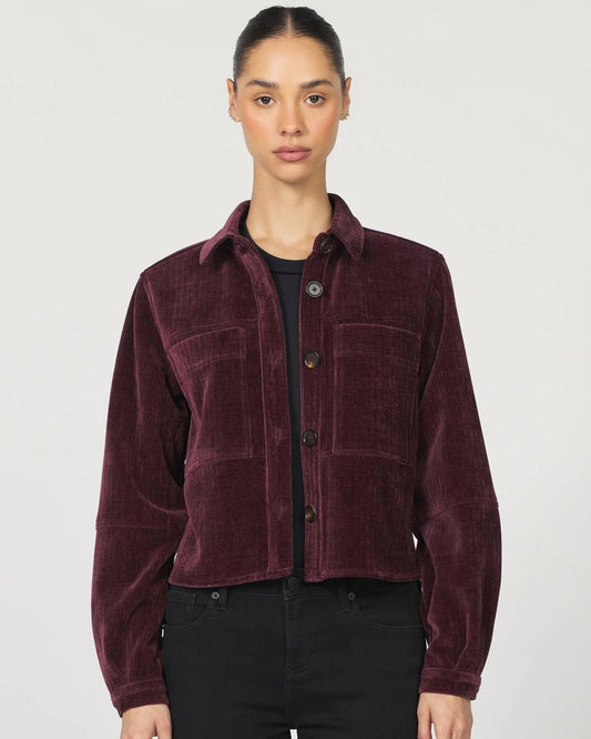 Woman wearing a burgundy corduroy shirt over a black top and pants on a white background