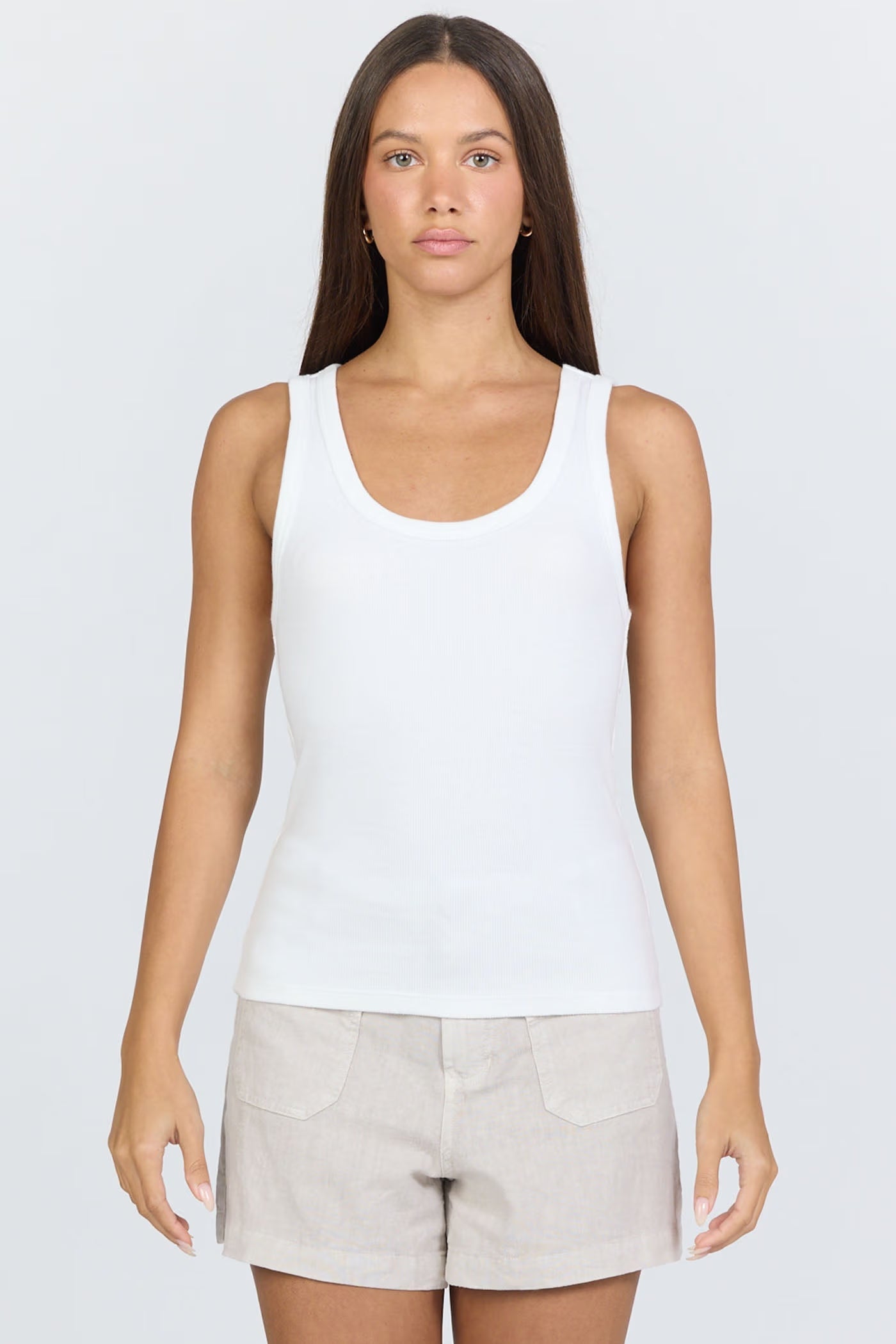Woman wearing a white tank top and beige shorts on a plain background