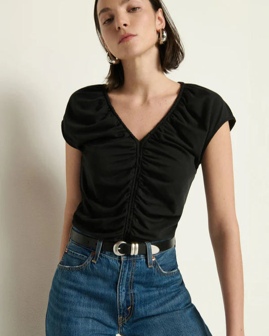 Woman wearing a black ruched top and blue jeans against a plain background