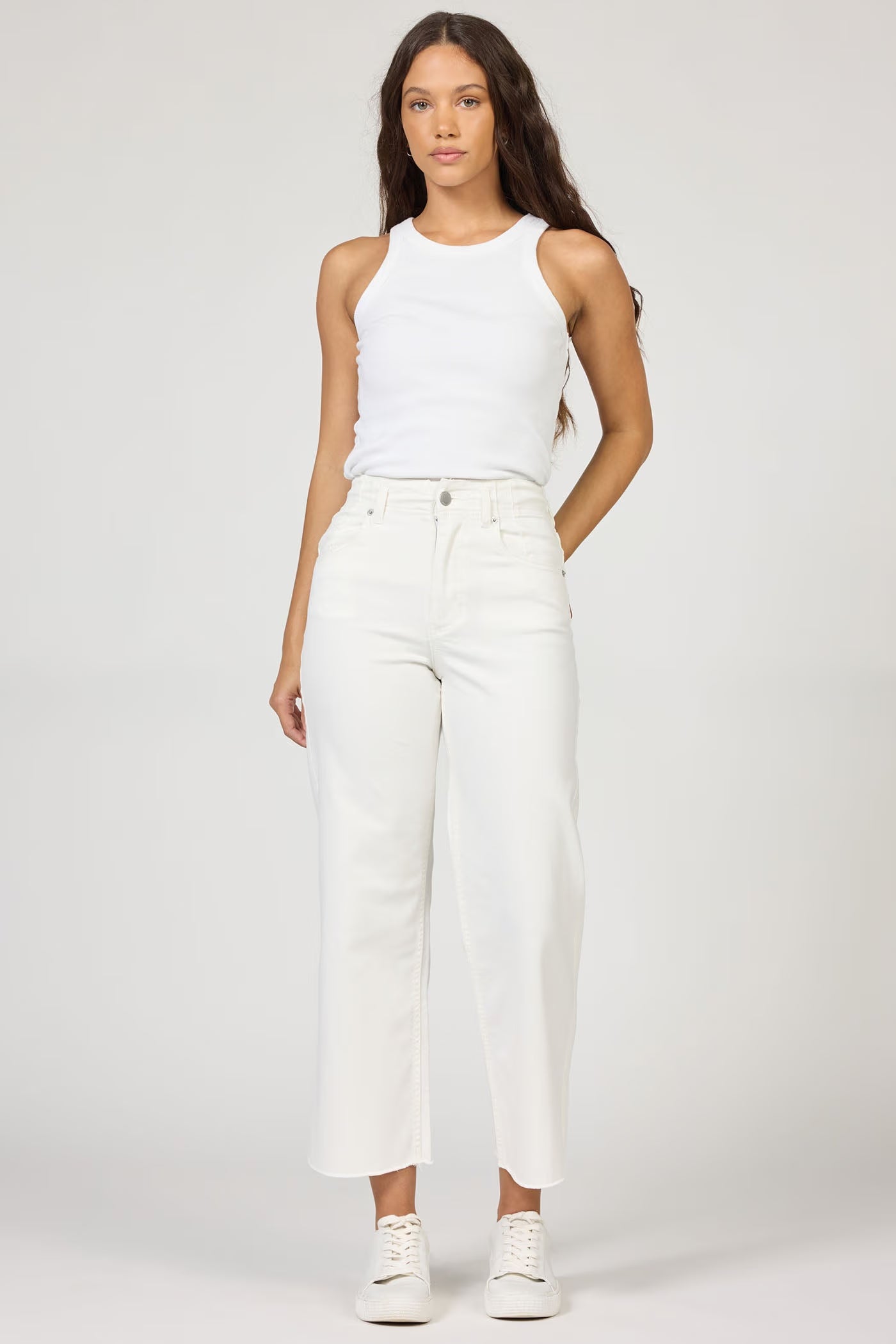 Woman wearing a white sleeveless top and white pants on a plain background