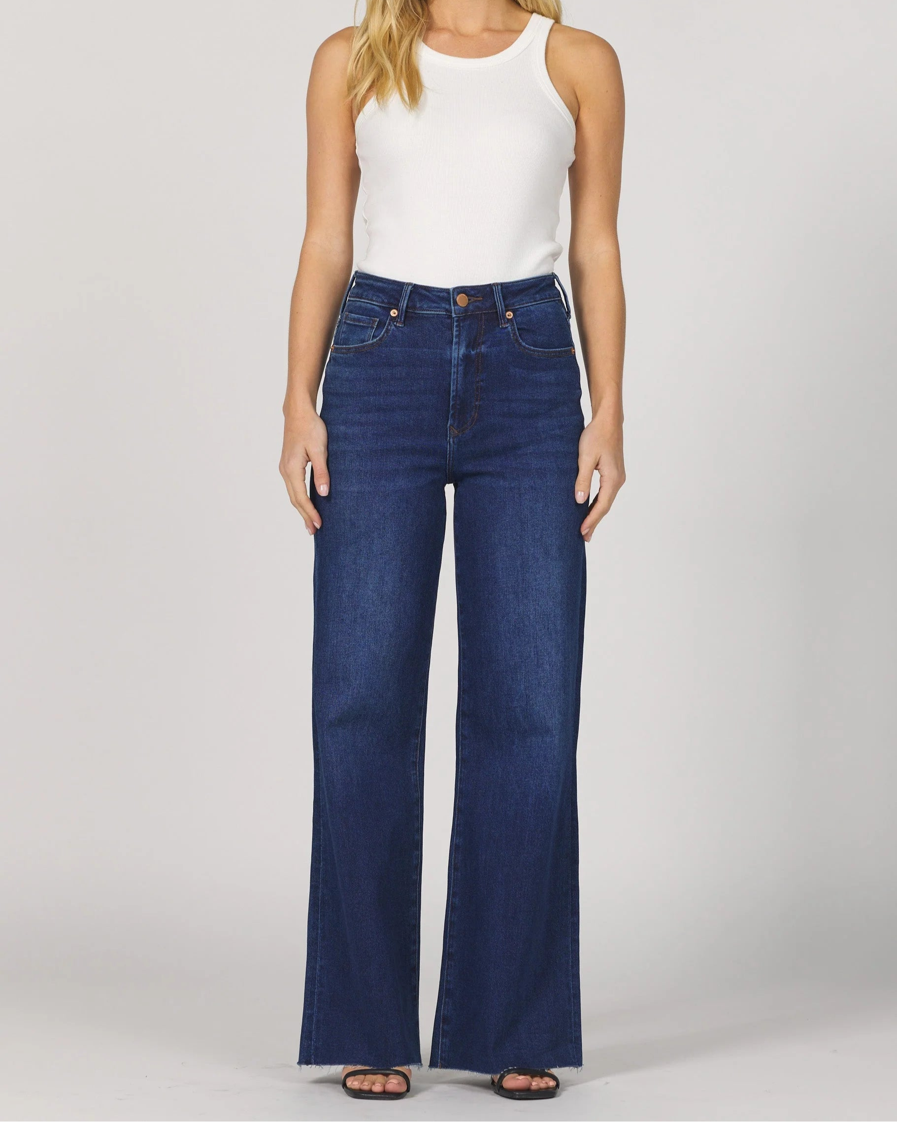 Woman wearing a white sleeveless top and blue jeans on a plain background