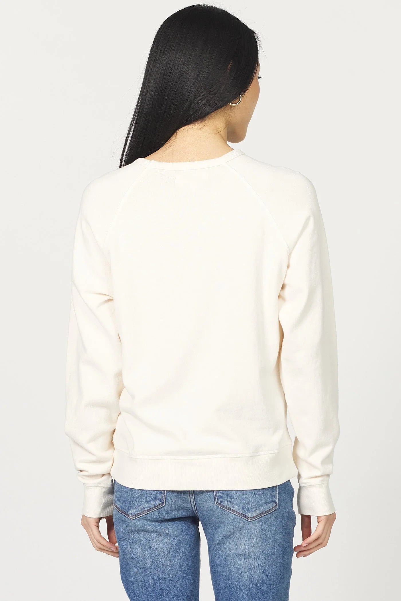 Person wearing a white sweater and blue jeans on a plain background