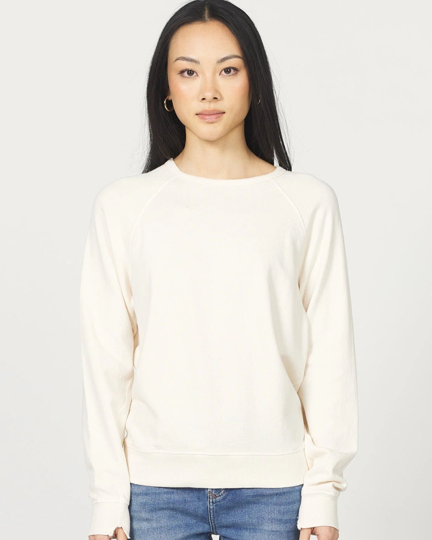 Woman wearing a cream sweater and blue jeans against a white background
