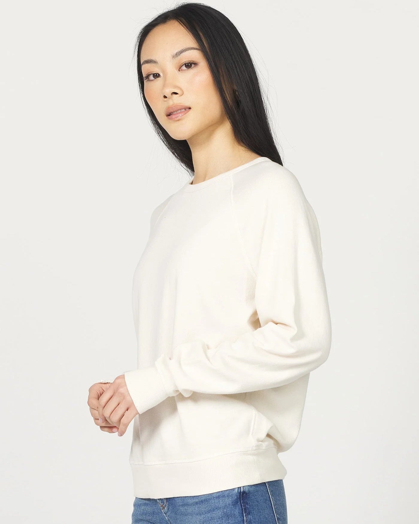 Woman wearing a white sweater and blue jeans on a plain background