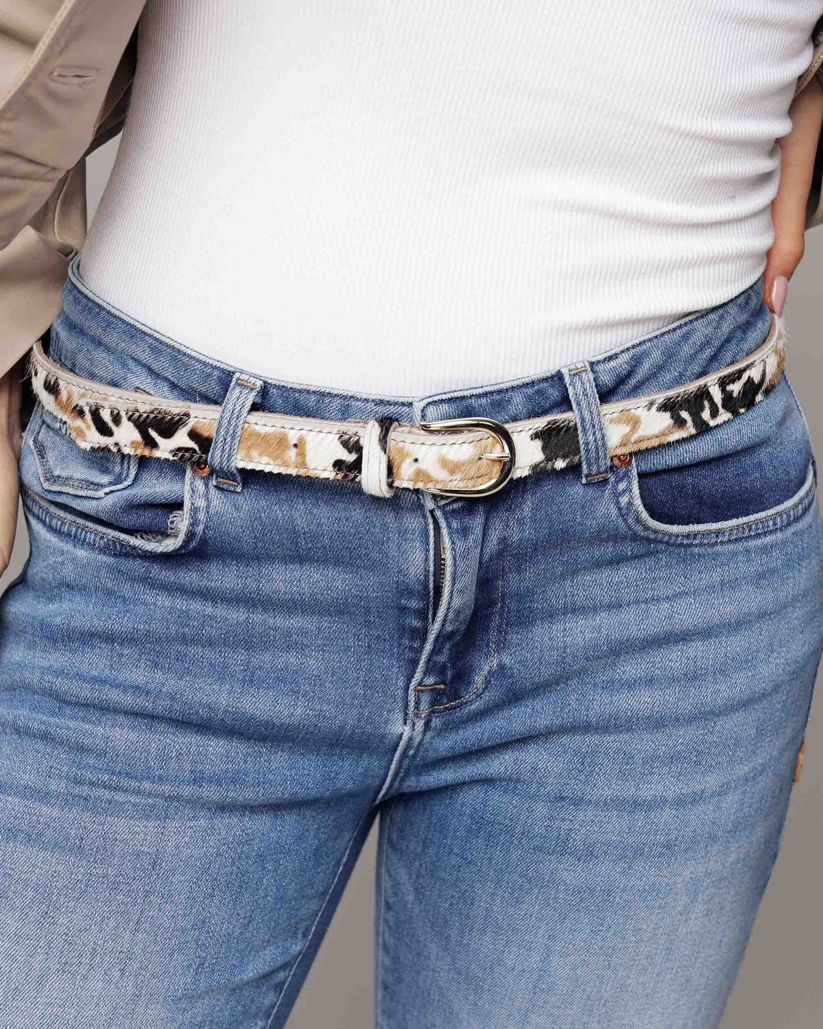A close-up of a model wearing a slim belt with a leopard print pattern in beige, brown, and black, paired with blue jeans and a white top.