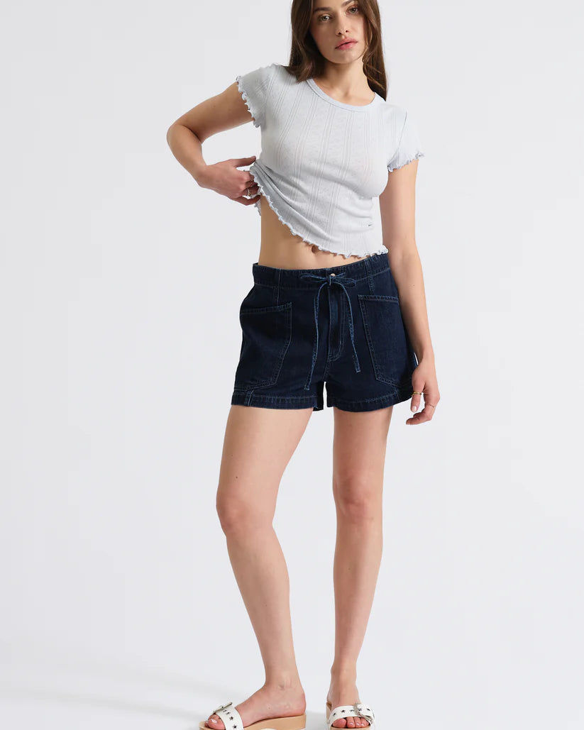 Woman wearing a white t-shirt and dark denim shorts on a light gray background