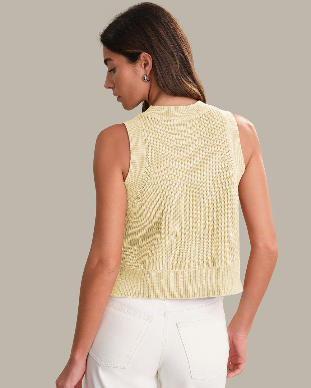 Woman wearing a light yellow sleeveless knitted top against a neutral background