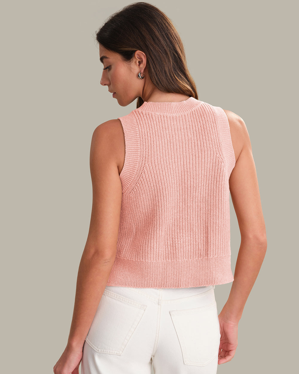 Woman wearing a pink knitted vest over a white top on a neutral background