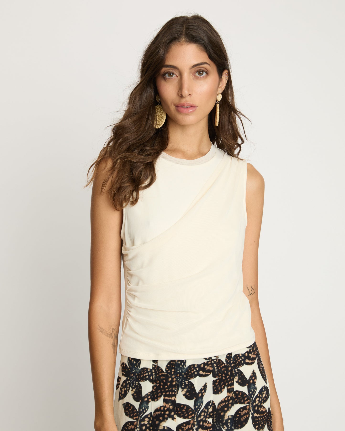 Woman wearing a sleeveless cream top and patterned skirt on a plain background